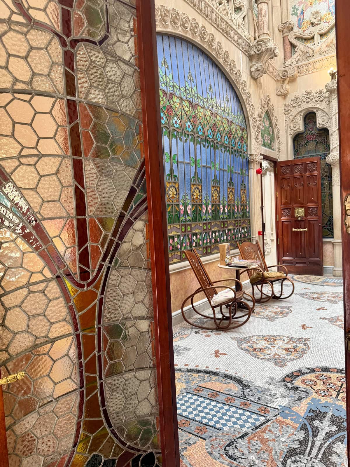 Inside a glamorous building with stained glass windows with two rocking chairs and elaborate design.