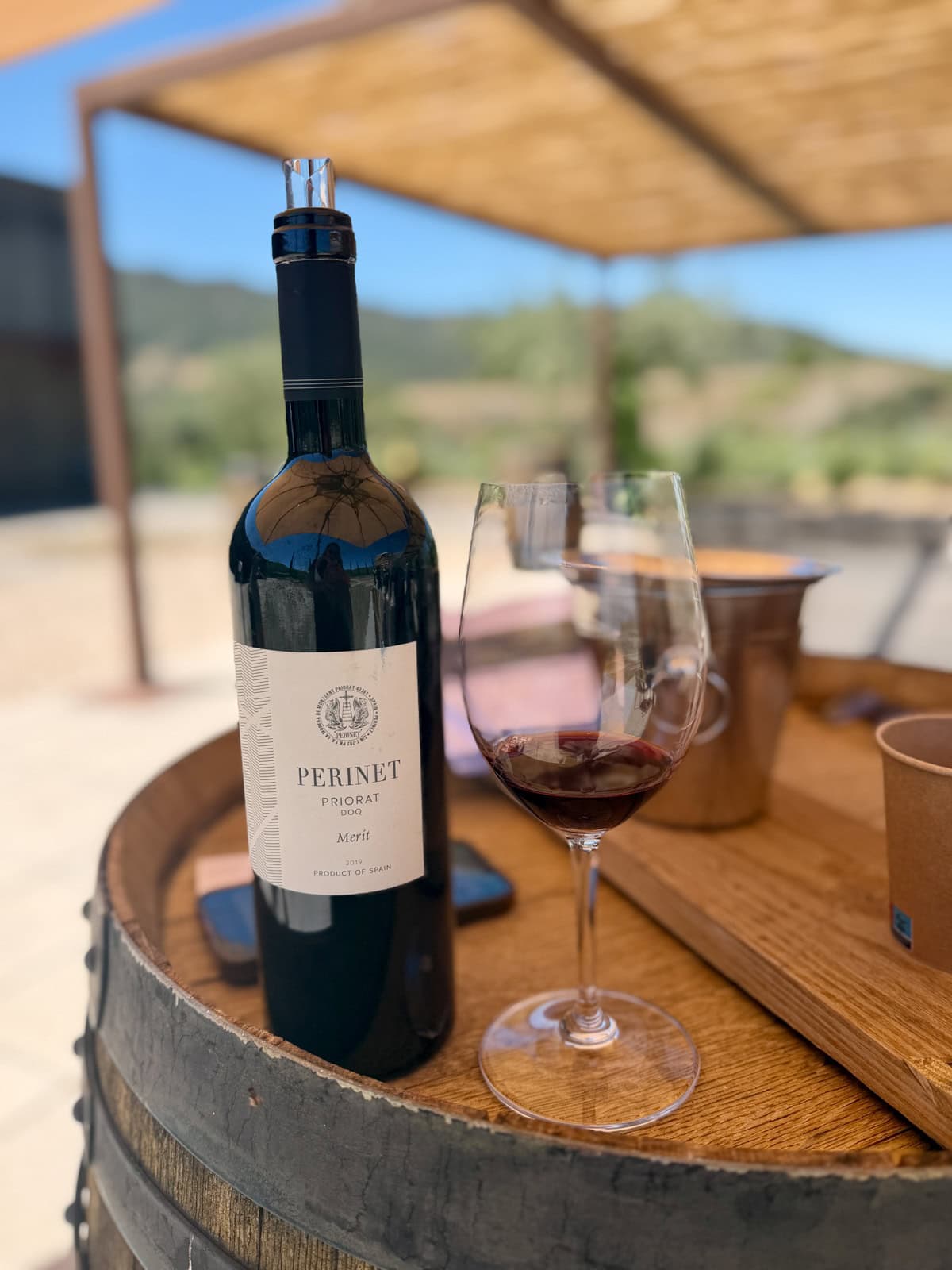 Bottle of wine next to a glass with a small amount of wine on top of a wine barrel.