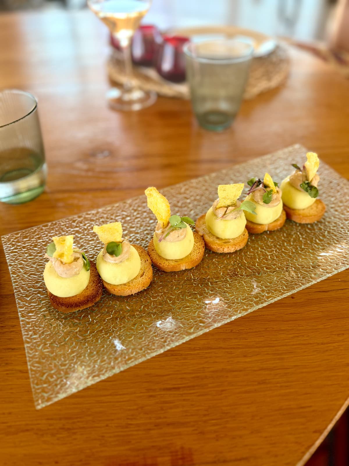 Yellow hors d'oeuvres on a glass platter on a wood table.