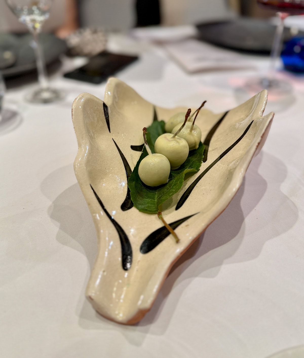 White chocolate covered cherries set of green leaves on a off white platter.