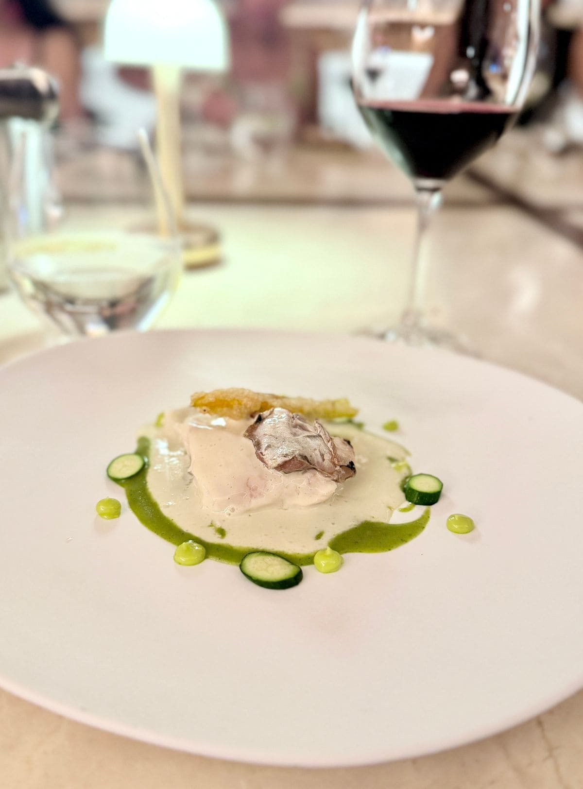 White fish on a plate with sauces and a glass of red wine in the background.