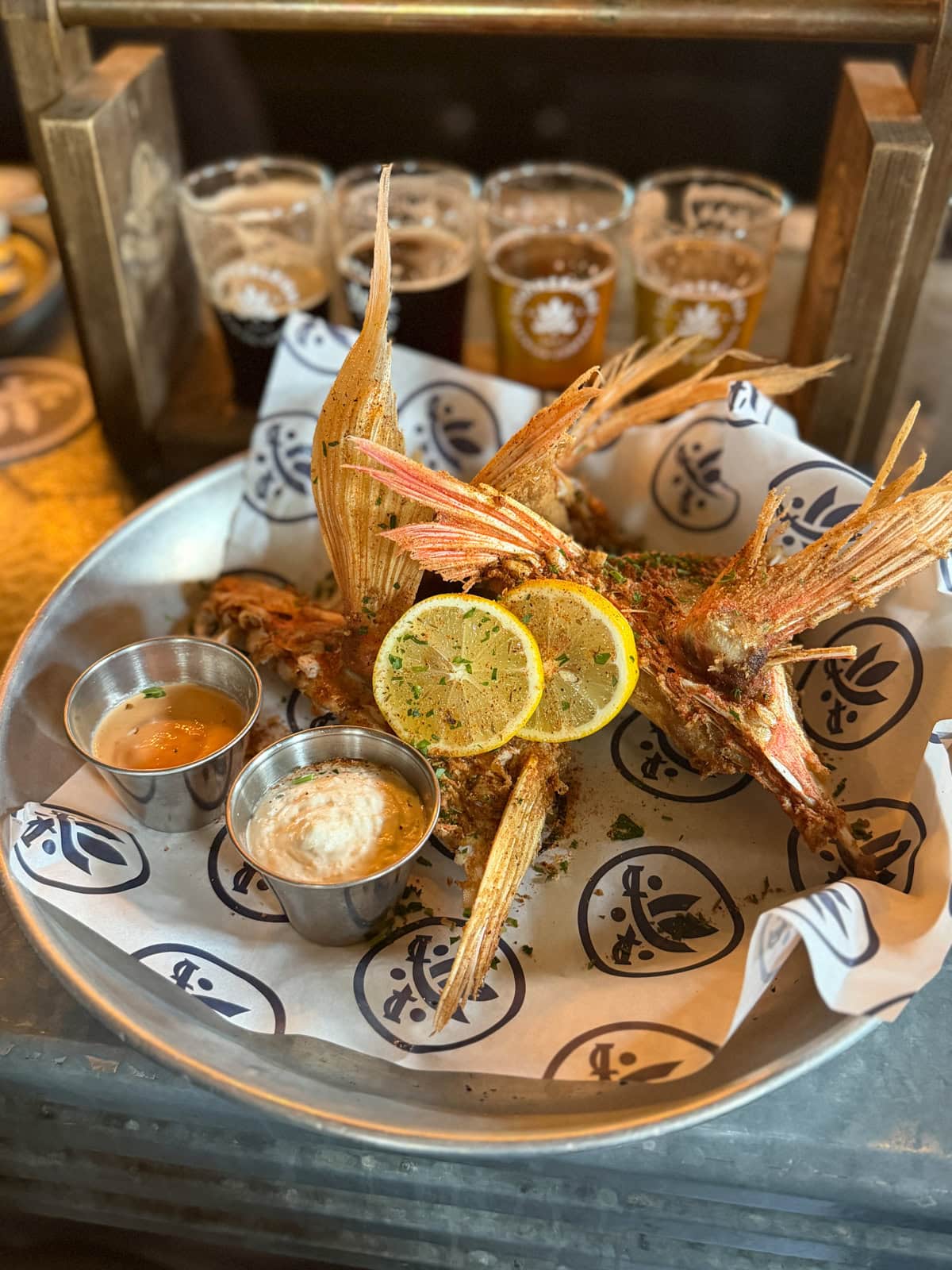 Fried fish with lemons and sauces on a silver plate with paper lining.
