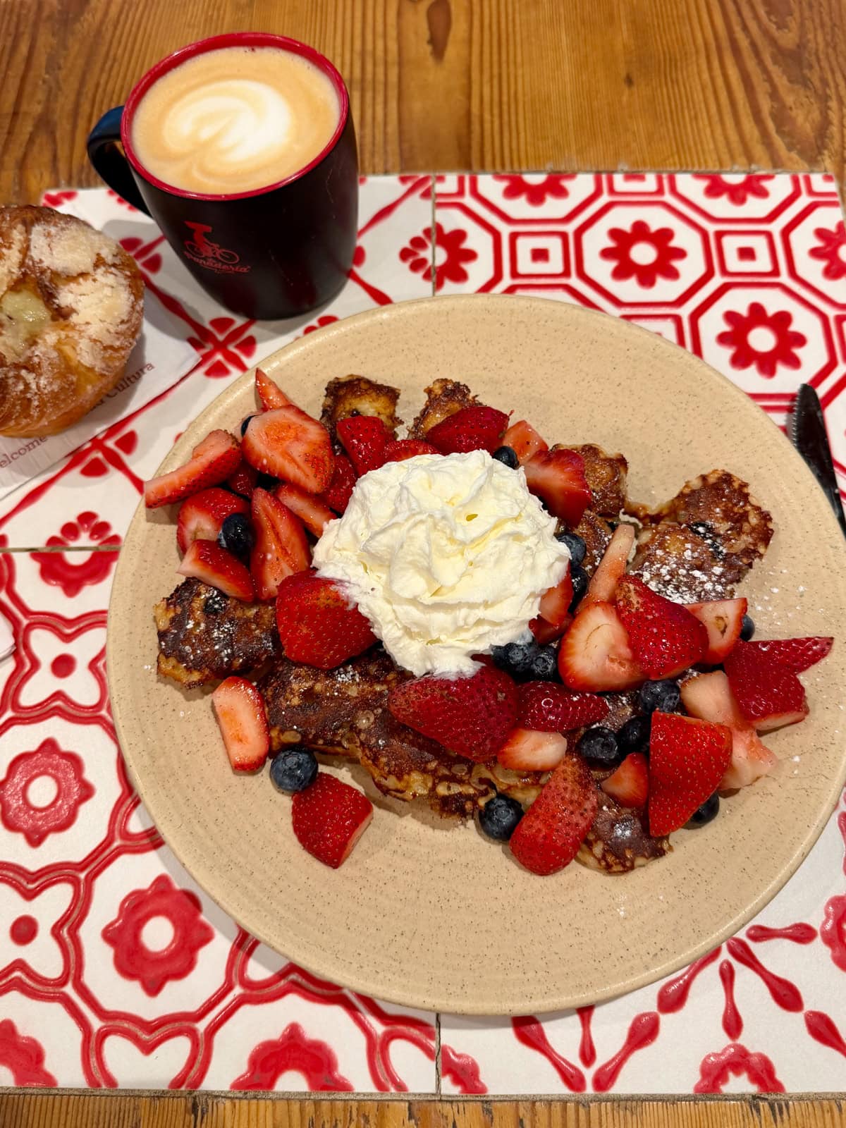 French toast with berries and whipped cream and a coffee and pastry on the side.